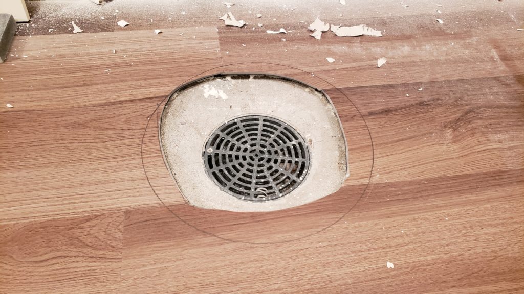 Vinyl flooring around a circular basement floor drain with sloppy, uneven edges.
