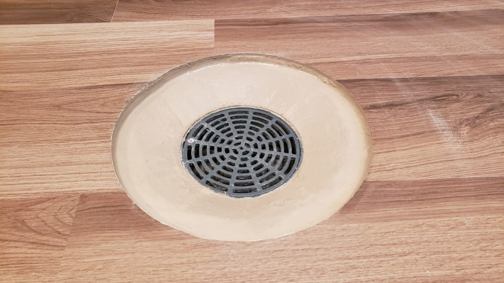 Vinyl flooring installed around a basement floor drain with perfectly circular finished edges.