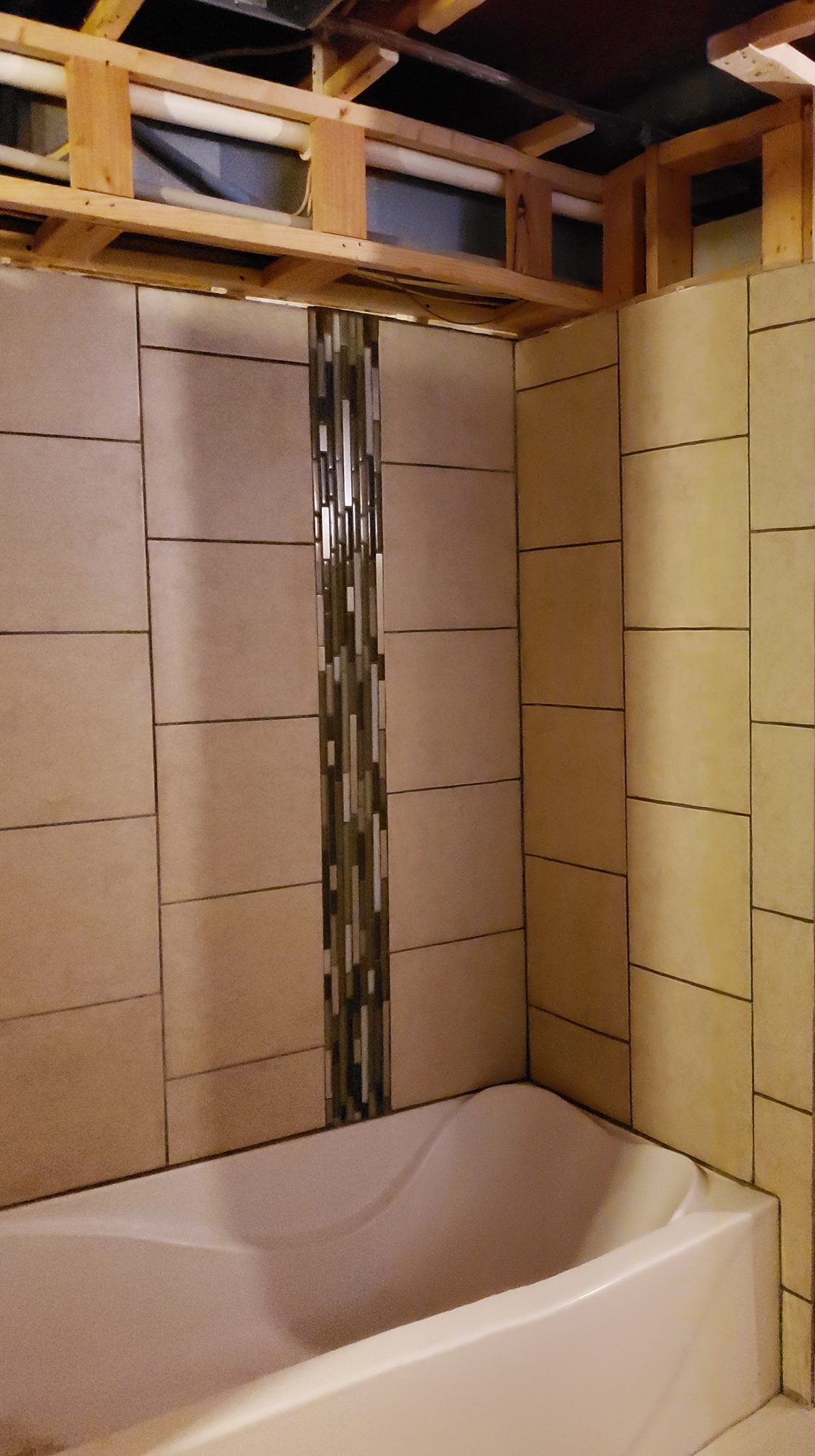 Tiled walls surround a bathtub in an otherwise unfinished basement.