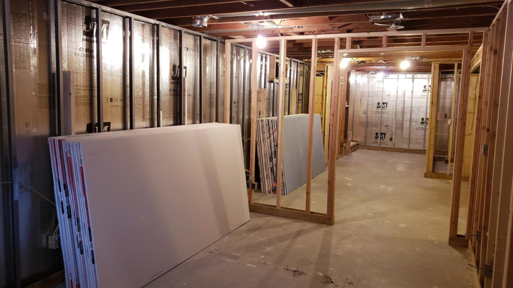 Stacks of drywall sheets leaning against basement wall framing.