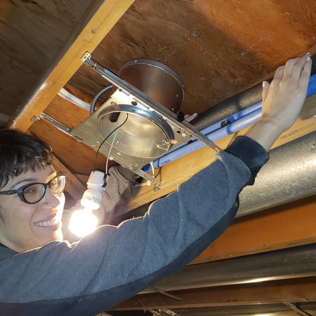 Installing pipe insulation over pex hot water pipes in a basement ceiling.