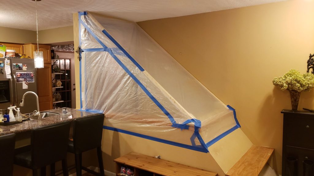 Controlling dust over an open stairwell with a cover made of a light wood frame covered with plastic sheeting and held together with blue tape.