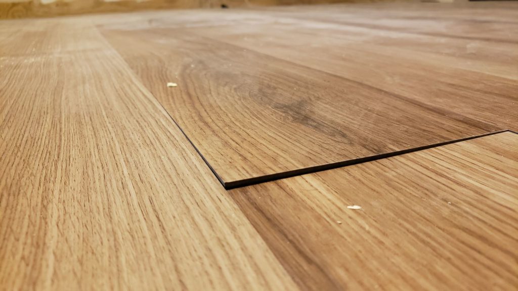 Wood grain vinyl flooring with a corner that has started to lift after installation.